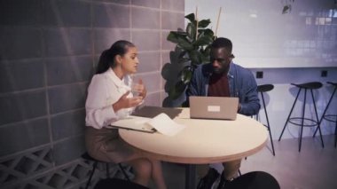 Netbook 'u olan iki çok ırklı iş arkadaşı ofiste iş projesi üzerinde çalışırken aynı masada oturuyorlar.