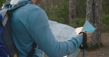 Sırt çantalı ve bastonlu isimsiz bir adamın, hafta sonu ormanda yürüyüş yaparken kağıt haritasını incelerken sağa dön.