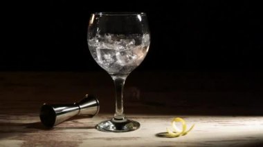 Buz küplerini limon ve jigger ile dolu bir bardak cin toniğine dolduran kişi karanlık odada.