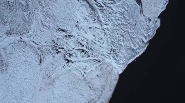 Soğuk kış gününde İzlanda 'da beyaz karla kaplı engebeli sakin karanlık denizin engebeli manzarası.