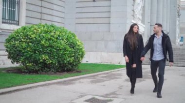 Şehrin kaldırımlarında yürürken el ele tutuşan, dış giyimli mutlu çift.
