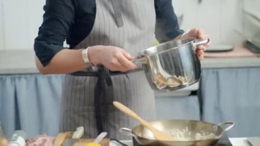 Önlüklü tanınmayan kadın aşçı pilav pişirirken tavada tavuk suyu ve pilav ekliyor.