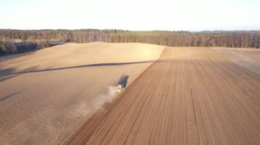 Gün batımında yemyeşil ağaçlarla çevrili tarımsal alanda traktörün sürüş görüntüsü.