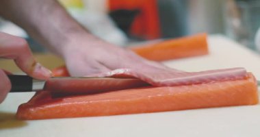 Geleneksel Japon restoranında suşi hazırlarken, isimsiz bir aşçının çiğ somon etini dilimleyişine odaklan.