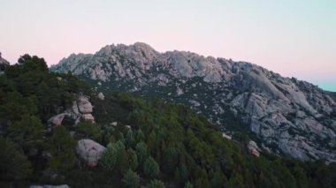 İspanya 'nın Sierra de Guadarrama kentindeki La Pedriza' da akşam saatlerinde gün batımına karşı uzanan dağ zirveleri ve yeşil ormanın nefes kesici manzarası.