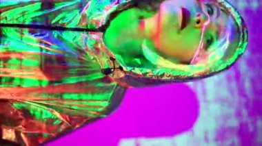 Akıllı artırılmış gerçeklik gözlüklü peruklu genç bir kadın. Sanal ekran görüntüleriyle stüdyoda parlak mavi ışıklarla dikilirken.