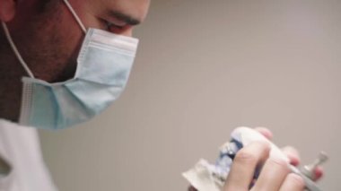 Laboratuvarda takma diş yaparken eklem makinesinde çenenin alçı kalıbını inceleyen konsantre erkek diş teknisyeninin yan görünümü
