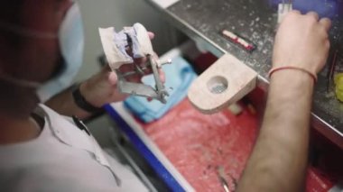 Yukarıdan gelen isimsiz erkek diş teknisyeni eklem makinesine takılı takma diş yapıyor ve alt çeneye seramik diş yerleştiriyor.