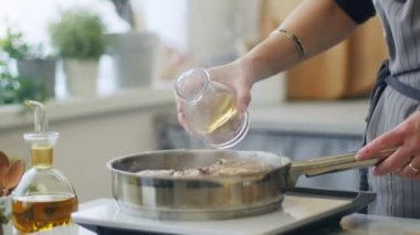 Gerçek zamanlı tanınmayan bir kadın elektrikli ocakta ossobuco pişirirken dana inciğiyle tavaya beyaz şarap ekliyor.