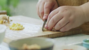 Ahşap kesme tahtasına sarımsak doğrayan kimliği belirsiz bir kadın. Yemek pişirme işlemi için gerekli malzemeleri hazırlarken.