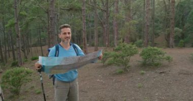 Sırt çantalı ve bastonlu bir adam hafta sonu ormanda yürüyüş yaparken kağıt haritayı inceliyor.