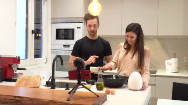 Birkaç pozitif blog yazarı salatayı yaparken akıllı bir telefondan evdeki hafif modern bir mutfakta mikrofonla özel ders videosu kaydediyor. 