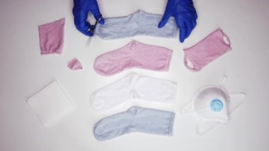 Mavi steril eldivenli meçhul kişiden pamuk çorabın içine beyaz peçete koyarken COVID 19 sırasında evde yüz maskesi yapıyor.