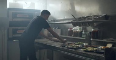 Erkek şefin domates soslu geleneksel İtalyan pizzası ve restoran mutfağında çeşitli malzemeler yaparken görüntüsü.