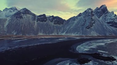 İzlanda 'da kış akşamları bulutlu gün batımına karşı karlı dağ sırtı manzarası.