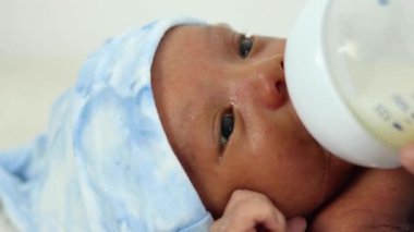 Kesilmiş, tanınmayan bir anne. Mavi battaniyeye sarılı süt şişesiyle sükuneti besleyen sevimli, yeni doğmuş bir bebek.