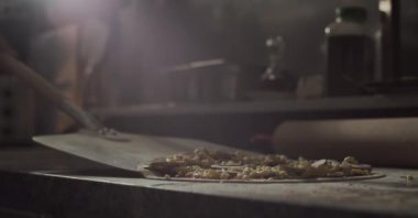 Metal kürekli isimsiz bir aşçı geleneksel İtalyan çiğ pizzasını mermer masa üstünden restoran mutfağında pişirmek için fırına götürüyor. 