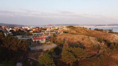 İspanya, Galiçya 'da dağlara ve günbatımına karşı deniz kıyısında yer alan Cangas do Morrazo kentinin nefes kesici insansız hava aracı görüntüsü