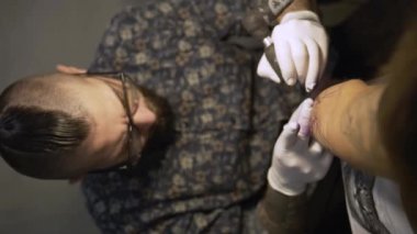 Stüdyoda genç bir kadının koluna dövme yapan dövme sanatçısı.