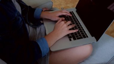 Genç bir bayanı kanepeye oturtup dizüstü bilgisayar kullanarak evde uzak bir projede çalıştırmak. 