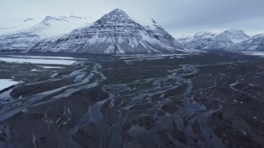Soğuk kış gününde İzlanda 'da, karlı dağ sırasının yakınındaki vadideki nehir haliçlerinin manzaralı manzarası.