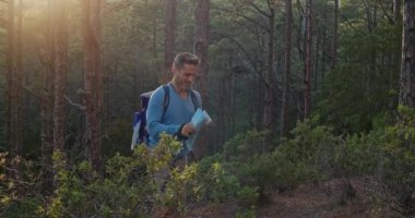 Sırt çantalı ve bastonlu bir adam hafta sonu ormanda yürüyüş yaparken kağıt haritayı inceliyor.