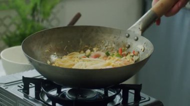 Meçhul bir kadının sebzeli Asya tavasına et suyu koyması ve mutfakta tavada kızartma pişirmesi.