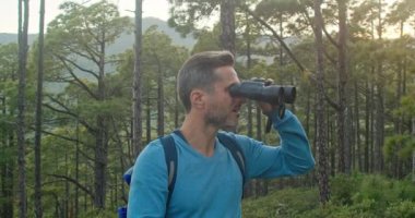 Sırt çantalı, mutlu, olgun erkek turistin bakışları altında dürbünle etrafa bakarken yaz haftasonunu ormanda geçiririz.