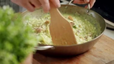 Yeni hazırlanmış risottoyla pastırmayı karıştıran isimsiz bir aşçı mutfaktaki ahşap tahtaya yerleştirilmiş.