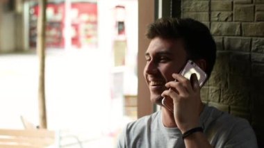 Neşeli genç adam kafenin penceresinin yanında akıllı telefondan konuşuyor.