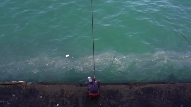 在黎巴嫩 在阳光灿烂的日子里 身着休闲装头戴便帽的男性渔民坐在破旧的石墩上 用鱼竿在波涛汹涌的海面上捕鱼 — 图库视频影像
