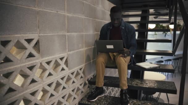 Konzentrierter Afroamerikanischer Arbeiter Mit Netbook Sitzt Auf Der Treppe Während — Stockvideo