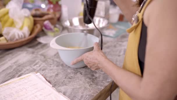 家庭用キッチンで食品を準備しながら 現代の電気ミキサーとボウルに成分を混ぜて作る認識できない女性の料理 — ストック動画