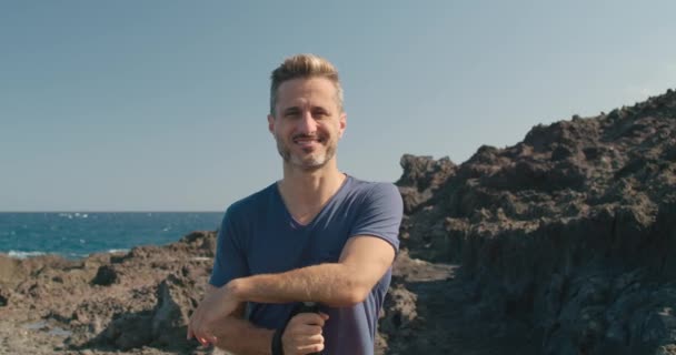 テネリフェ島 カナリア諸島 スペインの青い海と雲のない空に向かって火山の海岸に立っている間 ウォーキングスティックと笑顔でカメラを見る中年の男の周りのパン — ストック動画