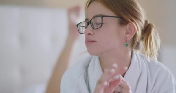 身穿白色浴衣 头戴眼镜 头戴钢笔的有思想的女学生 躺在床上做作业时 用手触摸下巴 — 图库视频影像