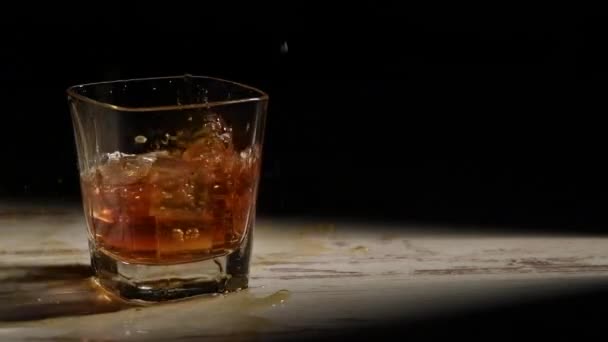 Person Hälla Isbitar Glas Med Bourbon Träbord Strålar Mot Svart — Stockvideo
