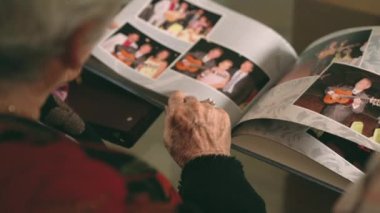 Yukarıdan gelen kadın koltukta oturuyor ve fotoğraf albümünden başka birine aile fotoğraflarını gösteriyor.
