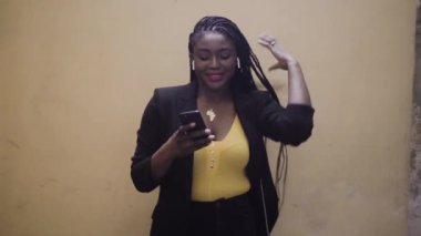 Siyah takım elbiseli Afro-Amerikan bir kadının akıllı telefonuyla sokakta dikilirken çekilmiş görüntüleri. 