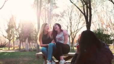 Kız arkadaşlar sonbaharda, günbatımında bir ormanda bankta oturuyorlar.