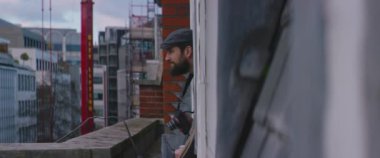 Neşeli genç hippi pencereden sarkıyor ve profesyonel fotoğraf makinesiyle fotoğraf çekiyor.
