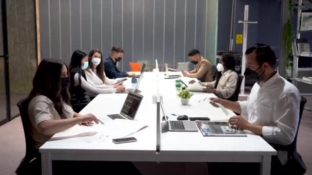 コロナウイルスパンデミック中にコワーキングスペースで働いている間 顔マスクとラップトップを使用してテーブルに座っている多様な人々の会社 — ストック動画