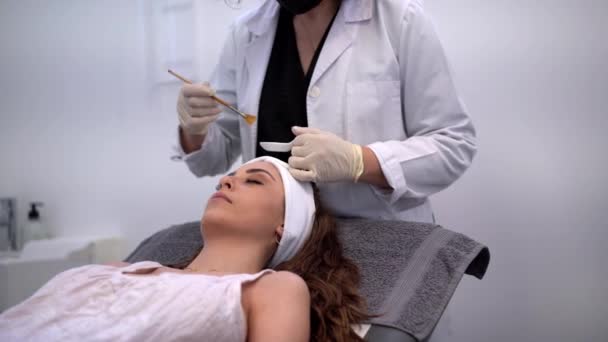 美容院的匿名作物美容师在女性病人的脸上涂酸剥脱 — 图库视频影像
