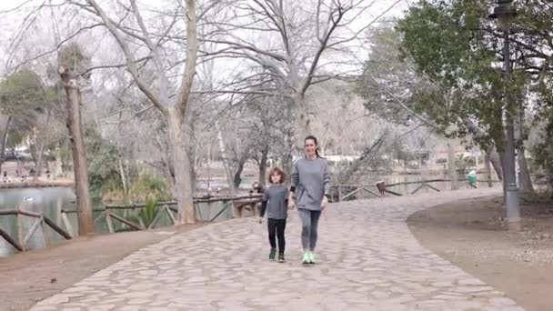 Matka Odzieży Sportowej Trzyma Chłopca Rękę Spacerując Chodniku Rozmawiając Drzewach — Wideo stockowe