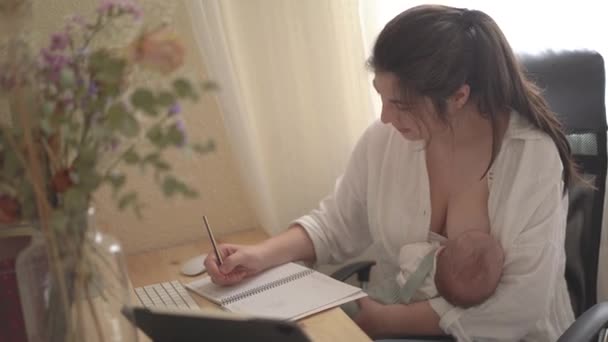 成年母亲白天在桌上的笔记本上记笔记时 用母乳喂养新生儿 — 图库视频影像
