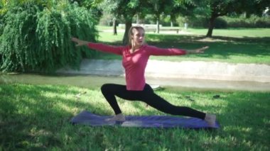Aktif giyimli, sportif bir kadın vücudu parkta pilates eğitimi sırasında hilal hareketi hareketleri ve yan esneme egzersizleri yapıyor.