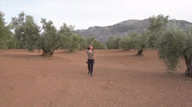 Canlı yeşil zeytin ağaçlarıyla çiftlikte yürürken akıllı telefonlu Asyalı kadın gezgin.