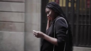 Siyah takım elbiseli genç Afrikalı Amerikalı bir kadının sokakta yürüdüğü görüntüler.  