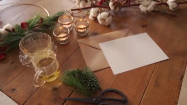 Noel kompozisyonu görüntüleri yanan mumlar ve boş kartpostalın yanına yerleştirilmiş çay fincanları köknar dalları ve pamuk dallarıyla süslenmiş tahta bir masa.
