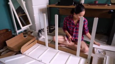 Yeni bir dairede mobilya montajı yaparken tüylü bir köpekle yerde oturan mutlu Asyalı kadın. 