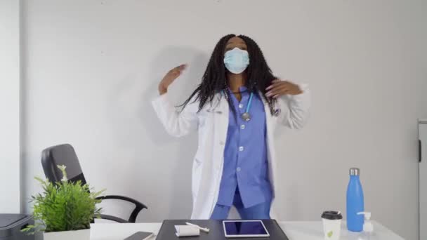休憩中に医師のオフィスでCovidダンスの広がりを防ぐための医療ユニフォームとマスクのアフリカ系アメリカ人女性 — ストック動画